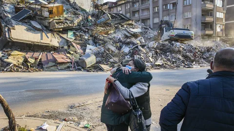 Twee vrouwen omhelzen elkaar voor ingestorte gebouwen
