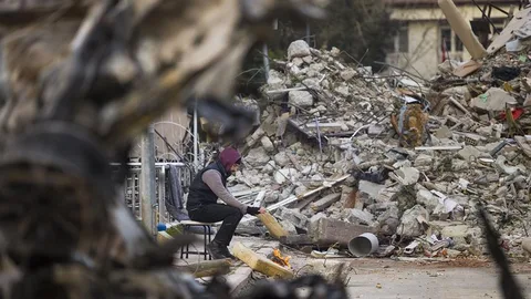 Een man zit op een kruk naast een ingestort gebouw