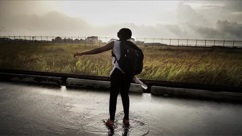 Blessing met een rugzak op haar rug staat in een plas water op straat.