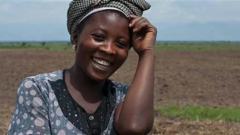 Een lachende vrouw met op de achtergrond akkerland.