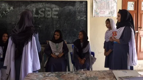 Een groep Pakistaanse meisjes zitten voor een schoolbord.