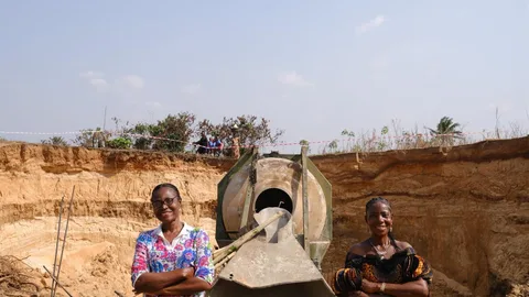 Virginia en een andere vrouw staan bij een brug in aanbouw in Nigeria.