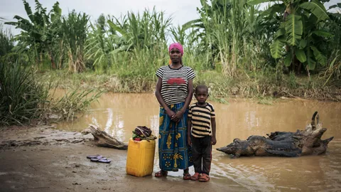 Rizini met haar kind en jerrycan voor het water bij een rivier.