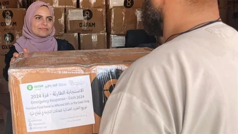 Een vrouw met hoofddoek geeft een doos met hulpgoederen aan een man.