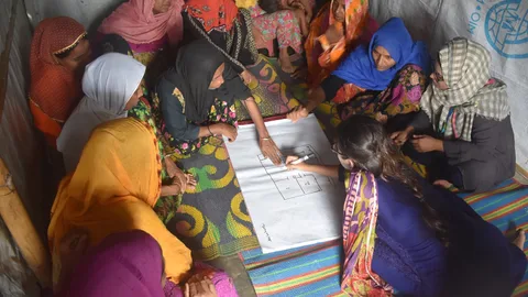 Een groep Rohingya-vrouwen zit in een kring met in het midden een plattegrond waarnaar enkele vrouwen wijzen.