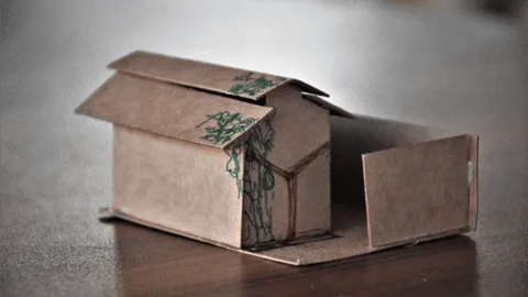 Een van papier gevouwen huisje met een boom erop getekend.