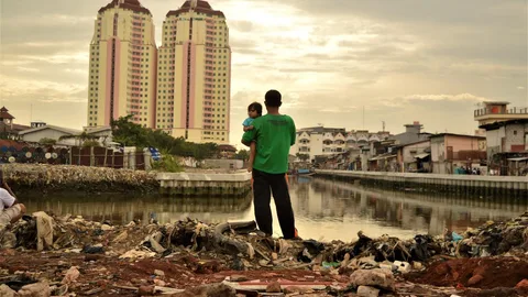 Foto van een vader die met zijn dochter de plek bezoekt waar hij vroeger woonde. In dit puin stond vroeger zijn huis, maar hij moest gedwongen vertrekken om ruimte te maken voor luxe appartementen. Het is tekenend voor de groeiende ongelijkheid in Indonesië. In Indonesië bezitten de 4 rijkste mannen meer dan de armste 100 miljoen mensen.