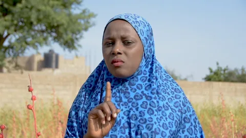 Een vrouw met een hoofddoek steekt haar wijsvinger op.