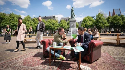 Dolf Jansen zit op een bank op het Plein in Den Haag en interviewt Kamerlid Azarkan (Denk).