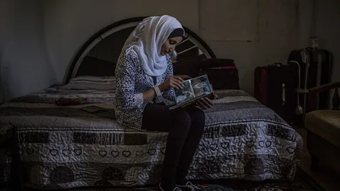 Fatem zit op een bed en bekijkt foto's.