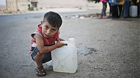 Een jongetje heeft net zijn jerrycan gevuld met water en rust even uit. Water is schaars en er is een constante rij mensen voor de waterkraan.