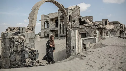 Foto van een vrouw, die tussen ruïnes loopt in Jemen