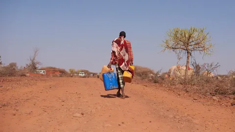 Een Ethiopiër loopt met drie jerrycans over een droge zandvlakte.