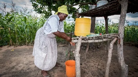 Zimbabwaanse boerin Marjory aan het werk met op de achtergrond een akker met gewassen.