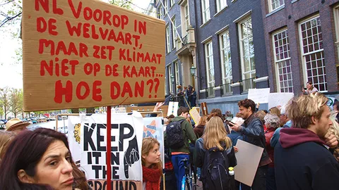 Demonstranten. Op een bord staat: NL voorop in de welvaart, maar zet klimaat niet op de kaart.. Hoe dan??