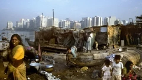 Mensen in een sloppenwijk met hoge gebouwen op de achtergrond.