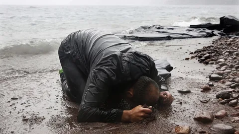 Een man knielt op het strand.