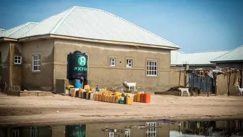 Een tank met het Oxfam logo en jerrycans bij een gebouw.