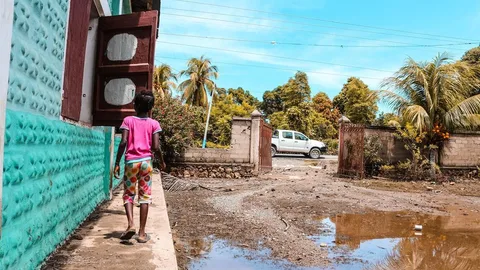 Klein kind in Haïti loopt langs een plas water op straat.
