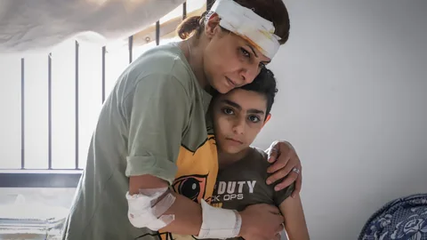 Huwaida heeft verband om haar hoofd en arm. Ze houdt haar zoon Ahmad vast.