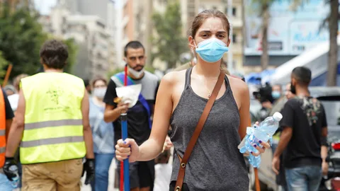 Een vrouw met een mondkapje en fles water in haar hand.