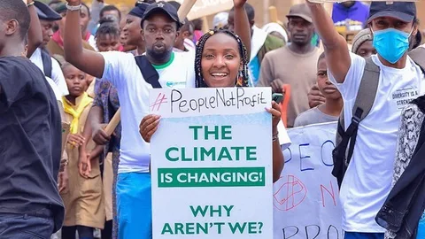 Elizabeth Wahtuti houdt tijdens een demonstratie een bord vast met de tekst: #PeopleNotProfit. The climate is changing! Why aren't we?