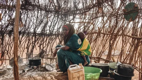 Sowda Omar Abdile uit Kenia zit bij een pan op het vuur en heeft een kindje op haar rug.
