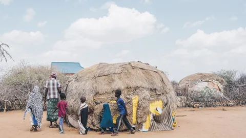 Omar loopt om een hut met achter hem een aantal kinderen.