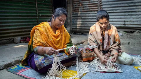 Photograph of two women weaving fabric