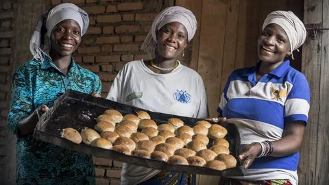 Three African women showing an oven plate with bread.