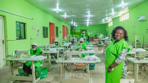 Olivia stands in a hall were seamstresses are at work.
