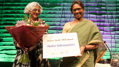 Malini Subramaniam holds a sign with her name for the Oxfam Novib PEN Award 2017. Farah Karimi stands next to her holding flowers.