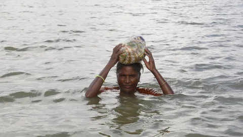 Een vrouw in Bangladesh staat tot haar nek in het water en houdt een voorwerp boven haar hoofd.