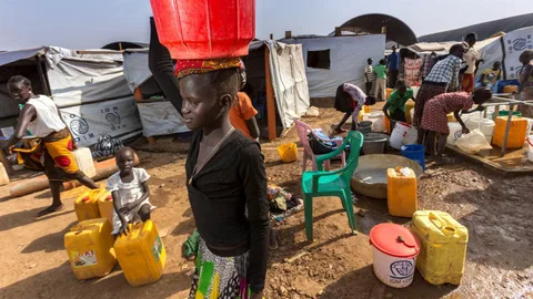 Mensen in een vluchtelingenkamp in Zuid-Sudan. Een meisje draagt een mand op haar hoofd.