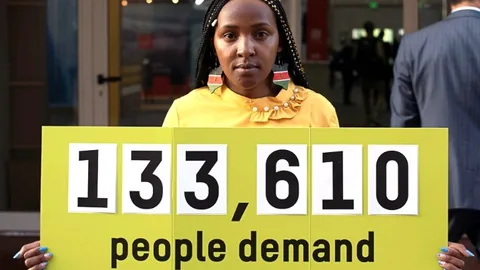 Elizabeth Wathuiti with a sign saying: 133,610 people demand loss and damage finance now.