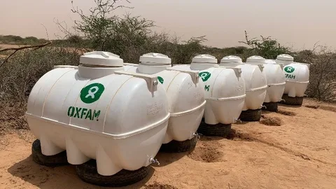 Watertanks met het Oxfam logo op een zandvlakte.