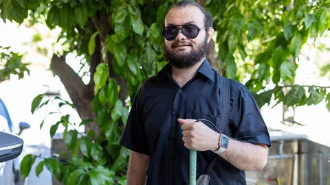Ahmad draagt een zonnebril en houdt een blindegeleidenstok vast.