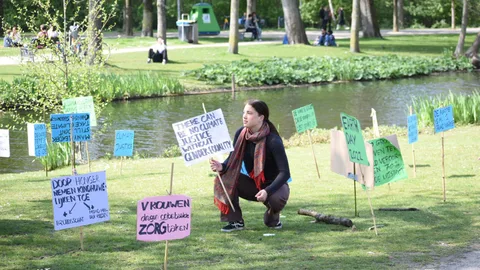 Een activist hurkt op het gras tussen protestborden