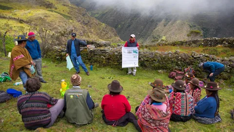 Mensen zitten op de grond in een kring en luisteren naar de presentatie.