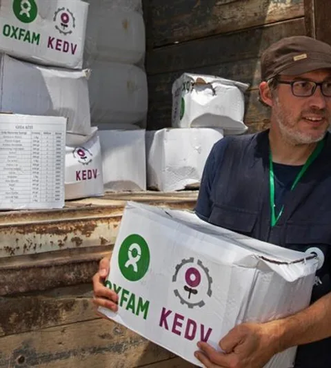 Een man laadt een doos met het Oxfam logo uit een vrachtwagen. Op de achtergrond staat een man met een hesje van Oxfam.