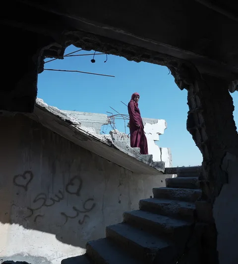 Een Palestijnse vrouw staat tussen gebombardeerde huizen in Gaza.
