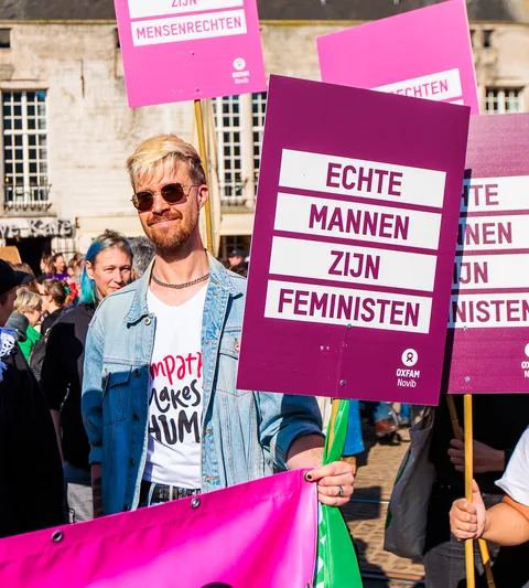Een mannelijke Oxfam-medewerker staat met een bord 'Echte mannen zijn feministen"