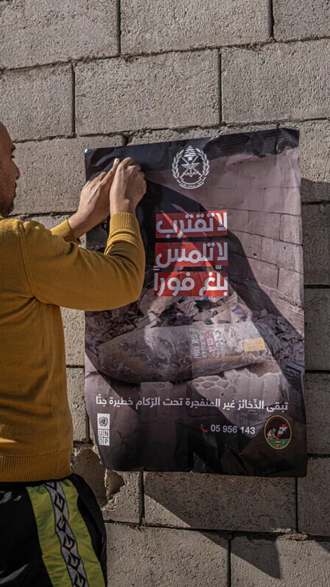 Saad plakt een poster met waarschuwing voor niet ontploft materiaal