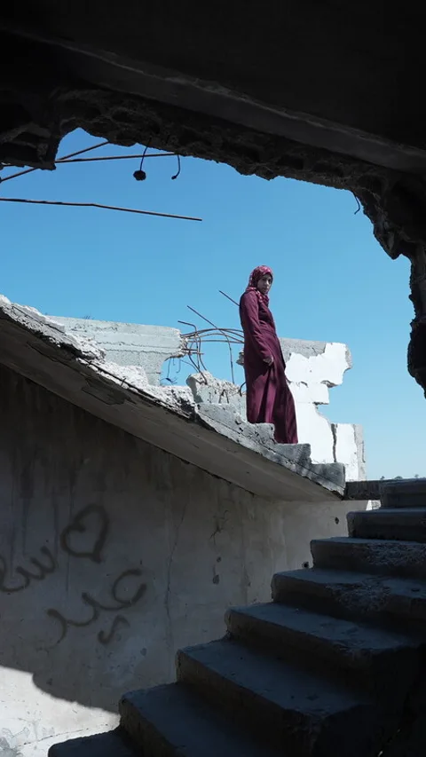 Een Palestijnse vrouw staat tussen gebombardeerde huizen in Gaza.